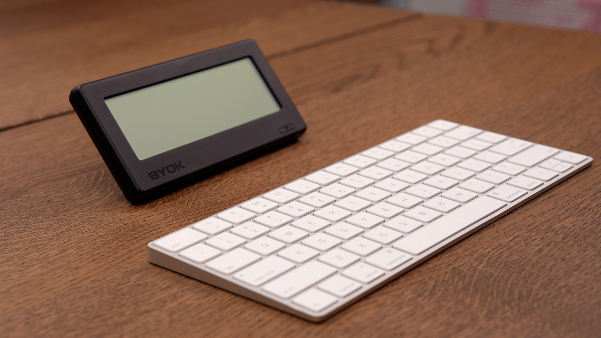 BYOK propped on its included stand next to an Apple Magic Keyboard on a wooden desk