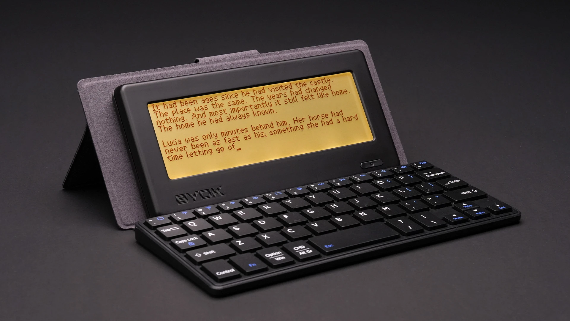 The BYOK writing device in its folio stand with a compact black keyboard, a story draft glowing on its amber screen